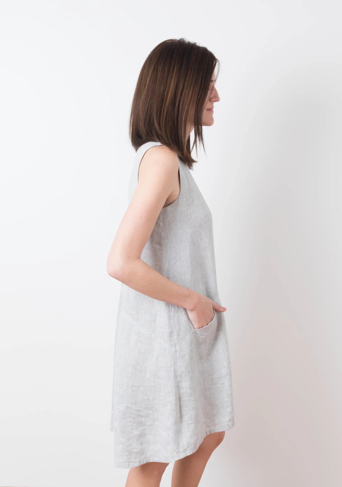 Model Kari is wearing a size 6 Farrow in a light colored linen fabric, side view sleeveless with pockets.
