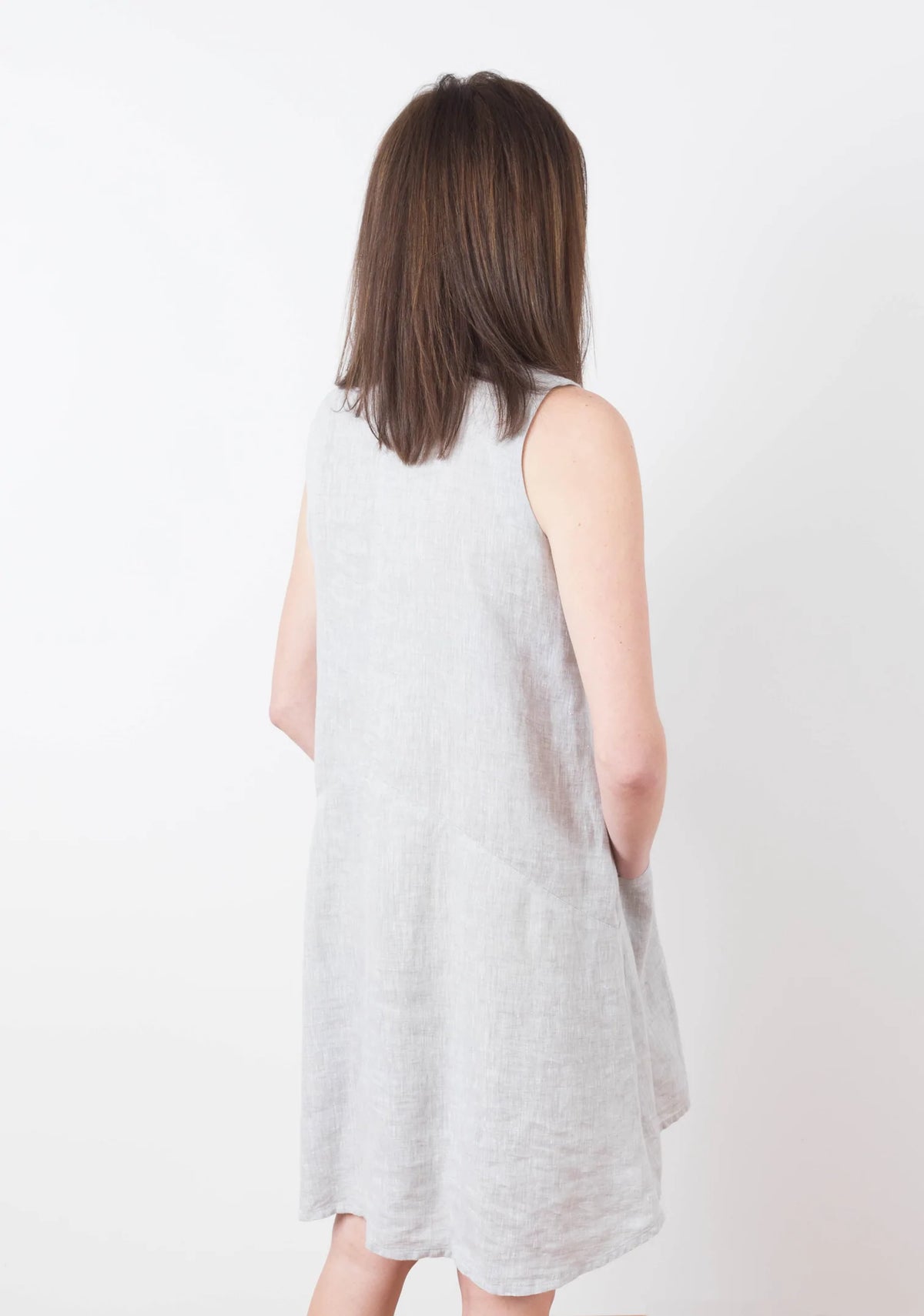 Model Kari is wearing a size 6 Farrow in a light colored linen fabric, back view sleeveless with pockets.